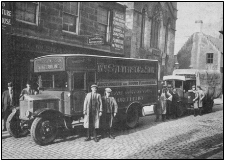 Photo of Stevenson’s shop & delivery vans in Bruce Street with founder William and son, Ian Stevenson (left) and van driver in forefront with other staff behind. c. 1928